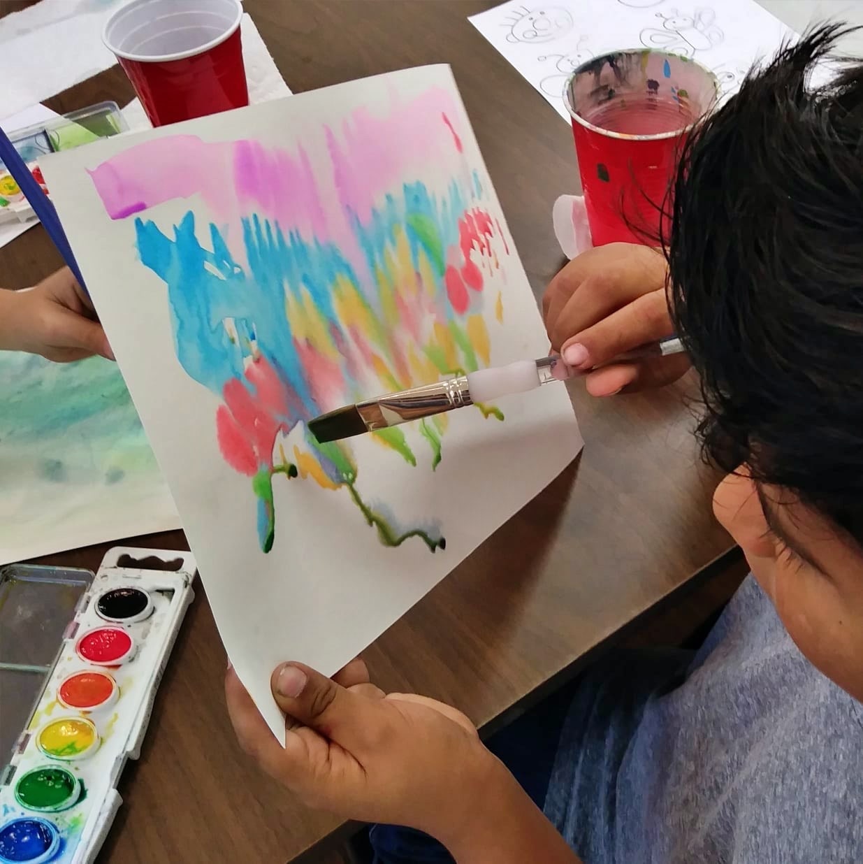Young boy painting water color on piece of white paper