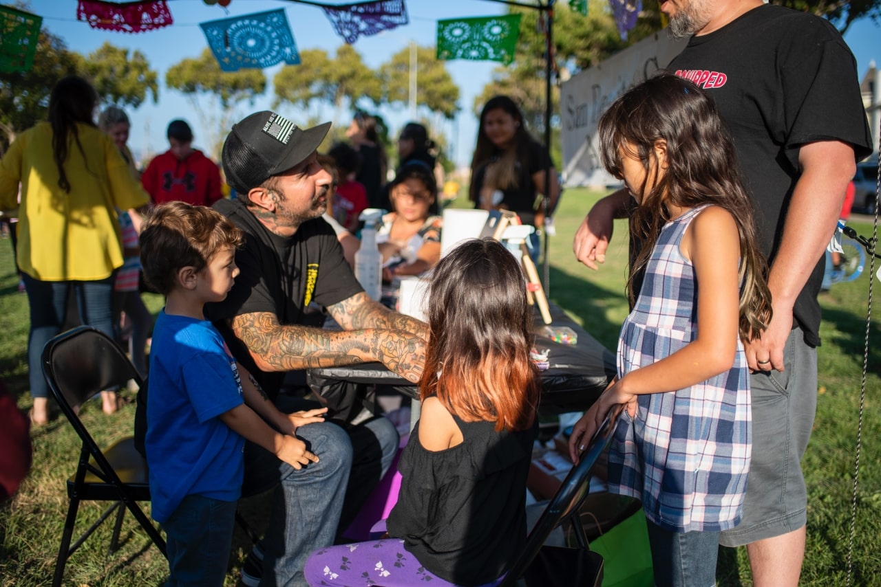 Kids and man with tattoos involved in outdoor art exhibition at city park in Hollister, California